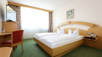 A hotel room with a bed, a desk, a chair, a telephone, and a painting on the wall.