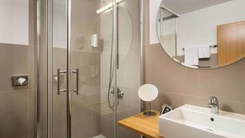 Un baño moderno con ducha de vidrio, tocador de madera con lavamanos y espejo redondo.