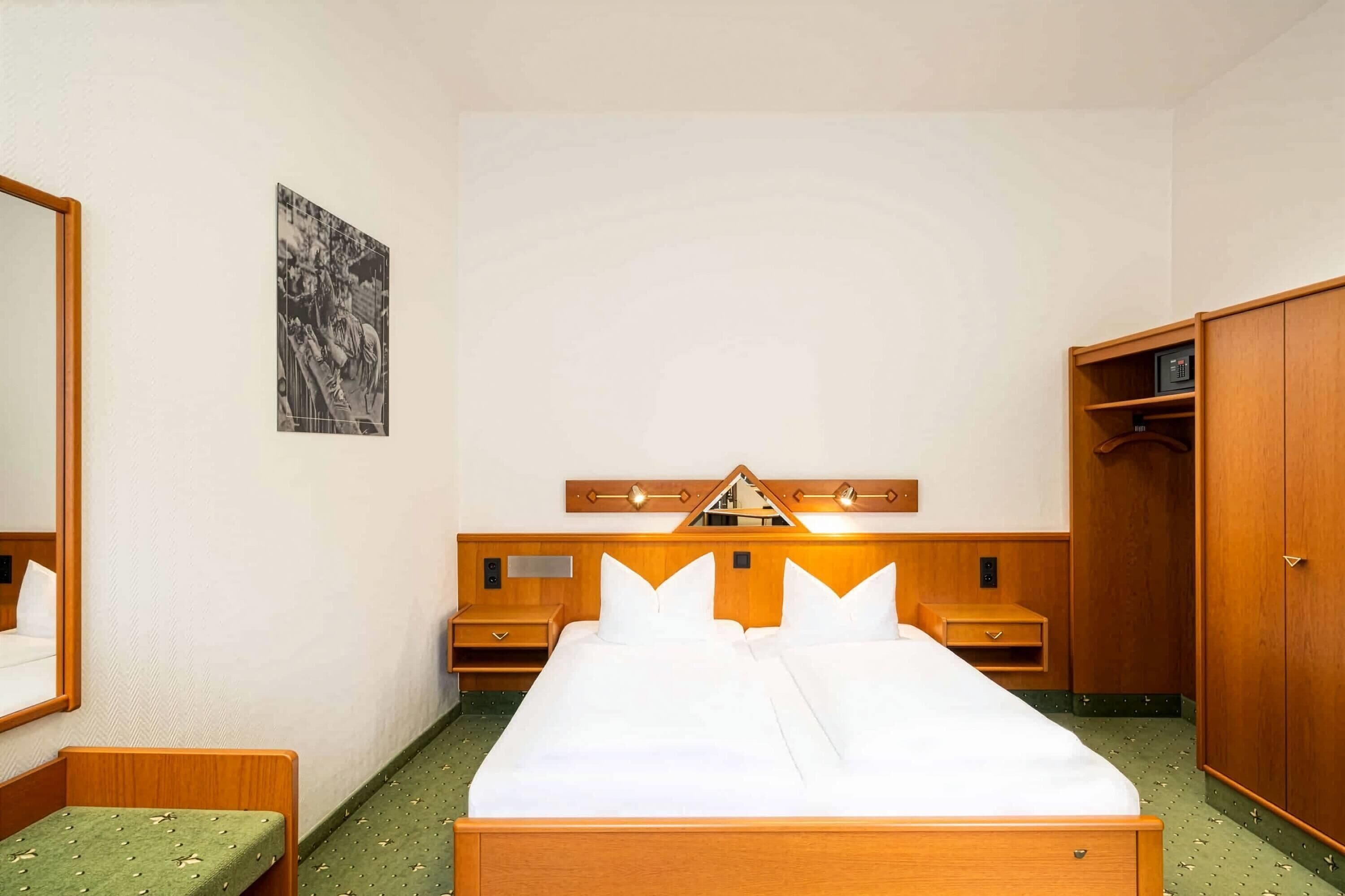 A hotel room with a large bed, wooden headboard, bedside tables, a wardrobe, and a framed picture on the wall.