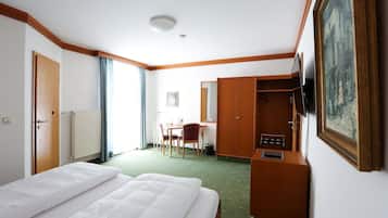 Una habitación de hotel con cama, escritorio, silla, armario y un cuadro en la pared.