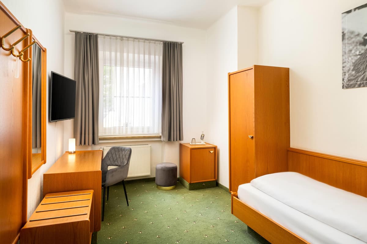 Ein Hotelzimmer mit Bett, Schreibtisch, Stuhl, Fernseher, Kleiderschrank und einem Fenster mit Vorhängen.