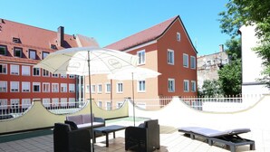 En utomhusplats med bord och stolar, en solstol och ett stort parasoll.
