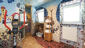 A bathroom with mosaic tile walls, a shower area, a wooden shelf with towels, and a red exercise machine. - Arthotel ANA Goggl, Trademark Collection by Wyndham (Landsberg am Lech)