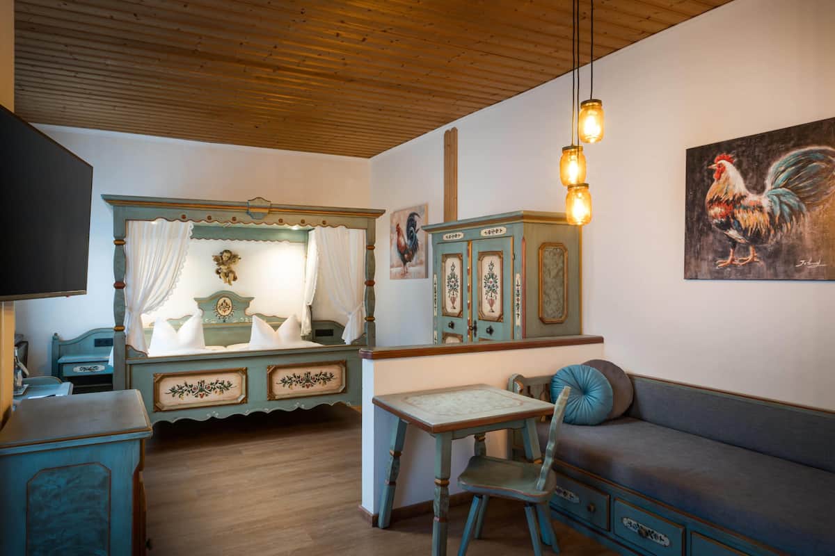 Ein Zimmer mit Holzboden, einem Tisch mit Stuhl, einer Couch und einem Schrank mit einem Hahn-Gemälde.