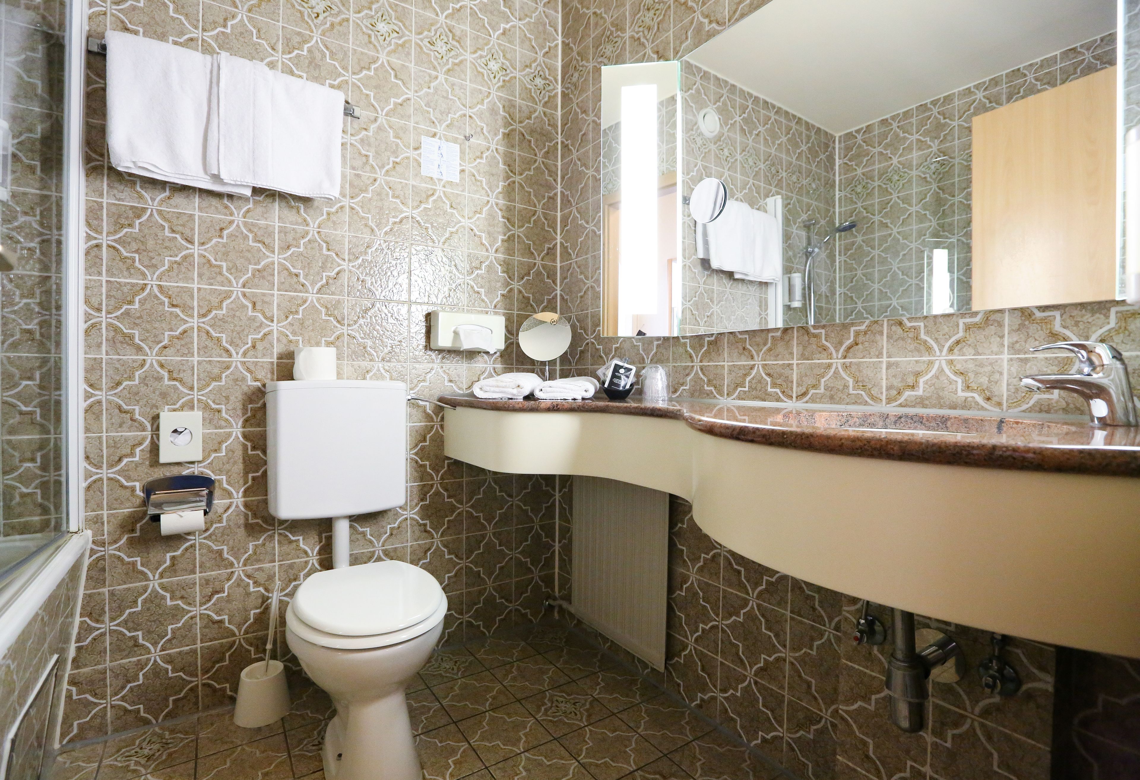Un baño con baldosas estampadas, un inodoro, un lavabo con espejo y un perchero para toallas.
