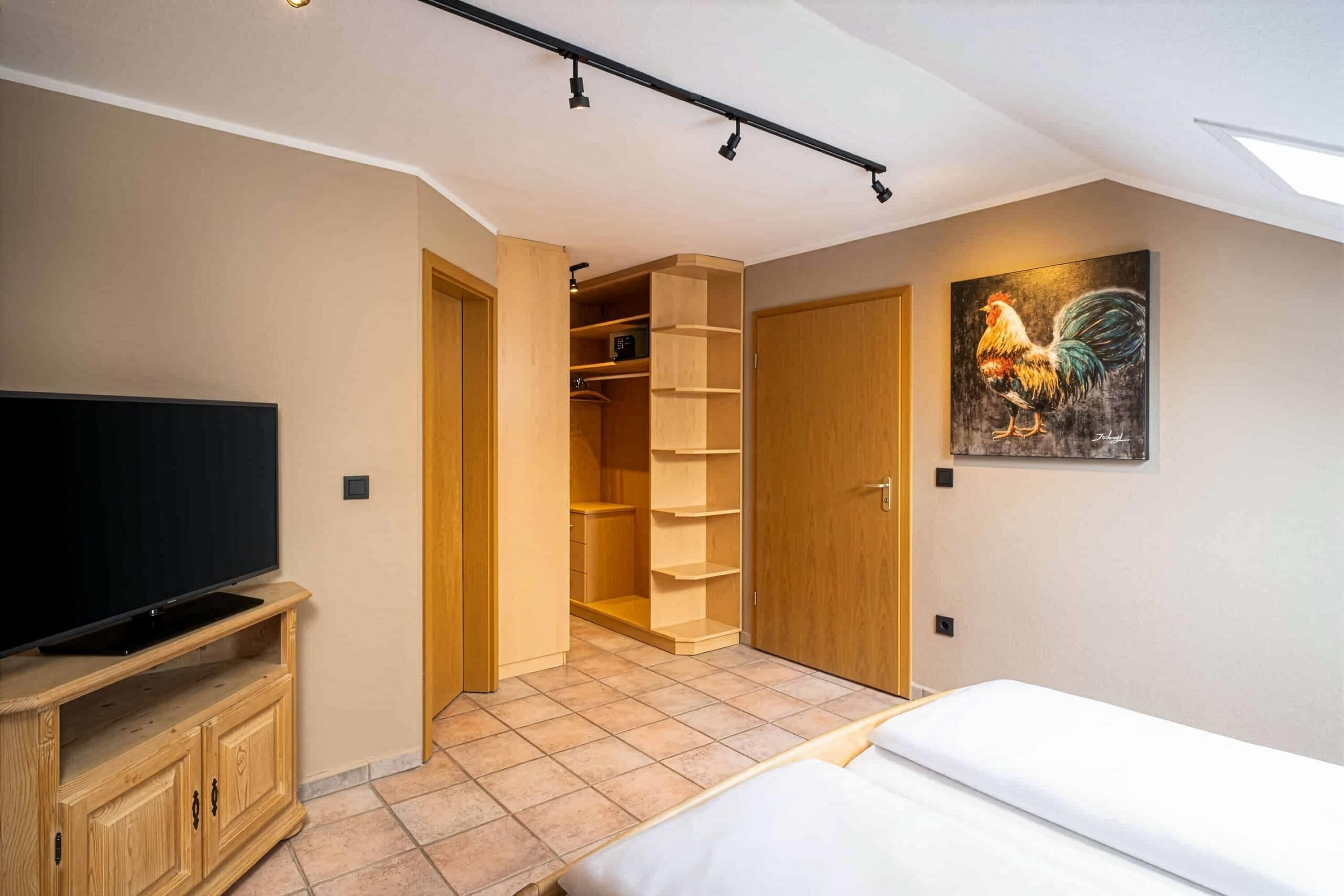 Una camera da letto con un letto, una TV, un guardaroba in legno, un armadio con ripiani e un quadro raffigurante un gallo.