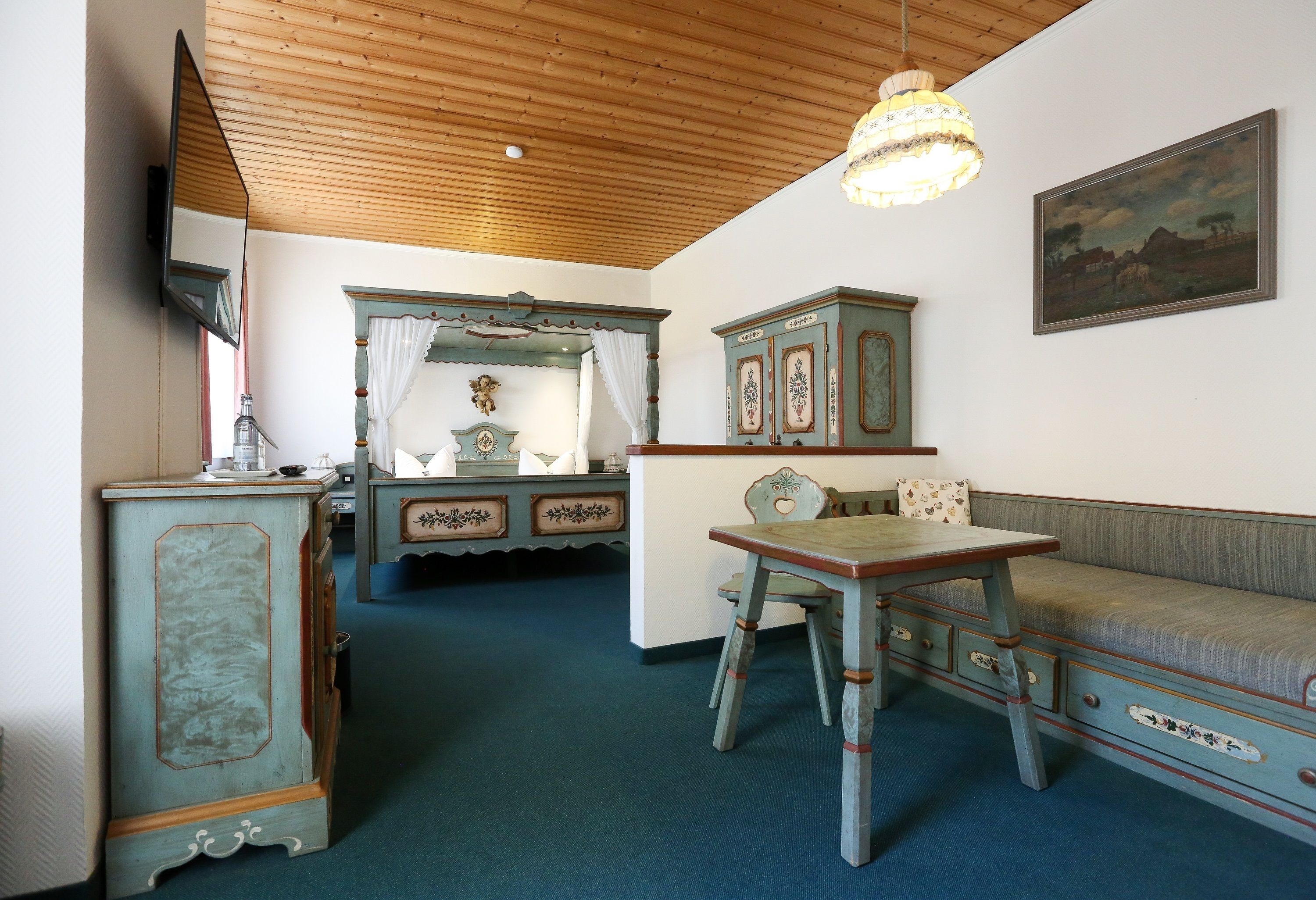 A room with a wooden ceiling, a dining table with chairs, a sofa, a cabinet with decorative elements, and a painting on the wall.