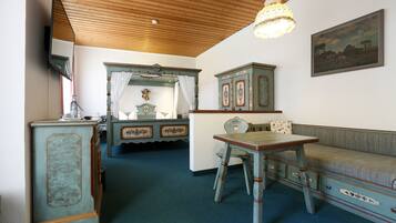 A room with a wooden ceiling, a dining table with chairs, a sofa, a cabinet with decorative elements, and a painting on the wall.