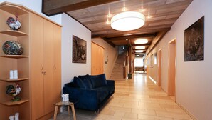 A hallway with a wooden ceiling, a blue sofa, a glass table, and a wooden wardrobe with decorative items. - Arthotel ANA Goggl, Trademark Collection by Wyndham (Landsberg am Lech)