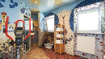 A room with a mosaic wall, a treadmill, a wooden shelf with towels, and a radiator.