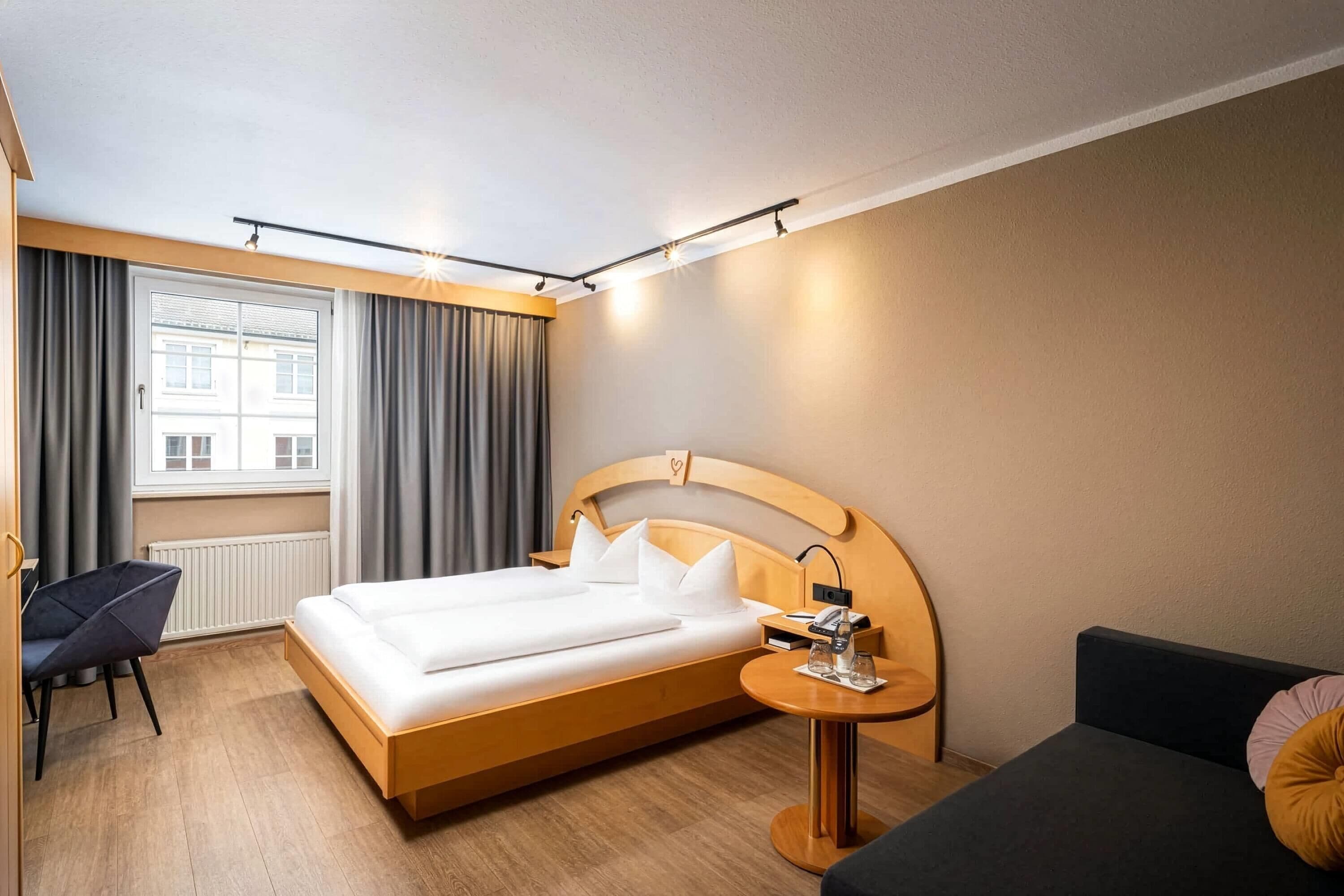 A hotel room with a bed, bedside table, chair, and a view of the outside.