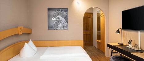 A hotel room with a bed, a desk, a chair, a television, and a framed picture on the wall.