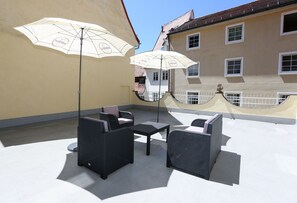 Un patio al aire libre con mobiliario de mimbre y dos sombrillas blancas.