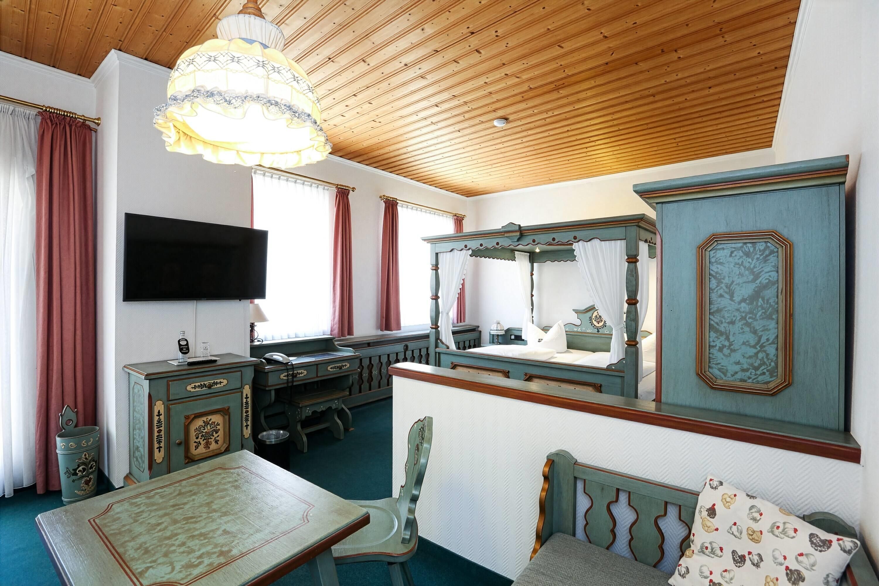 Una habitación con techo de madera, televisor, cama con dosel, escritorio con cajones, una silla y una mesa.