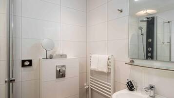 Een moderne badkamer met een douchecabine van glas, een wit wastafeltje met spiegel en een handdoekrek.