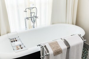 Un baño moderno con una bañera independiente, un perchero con una toalla doblada y un portabotellas en el borde de la bañera.