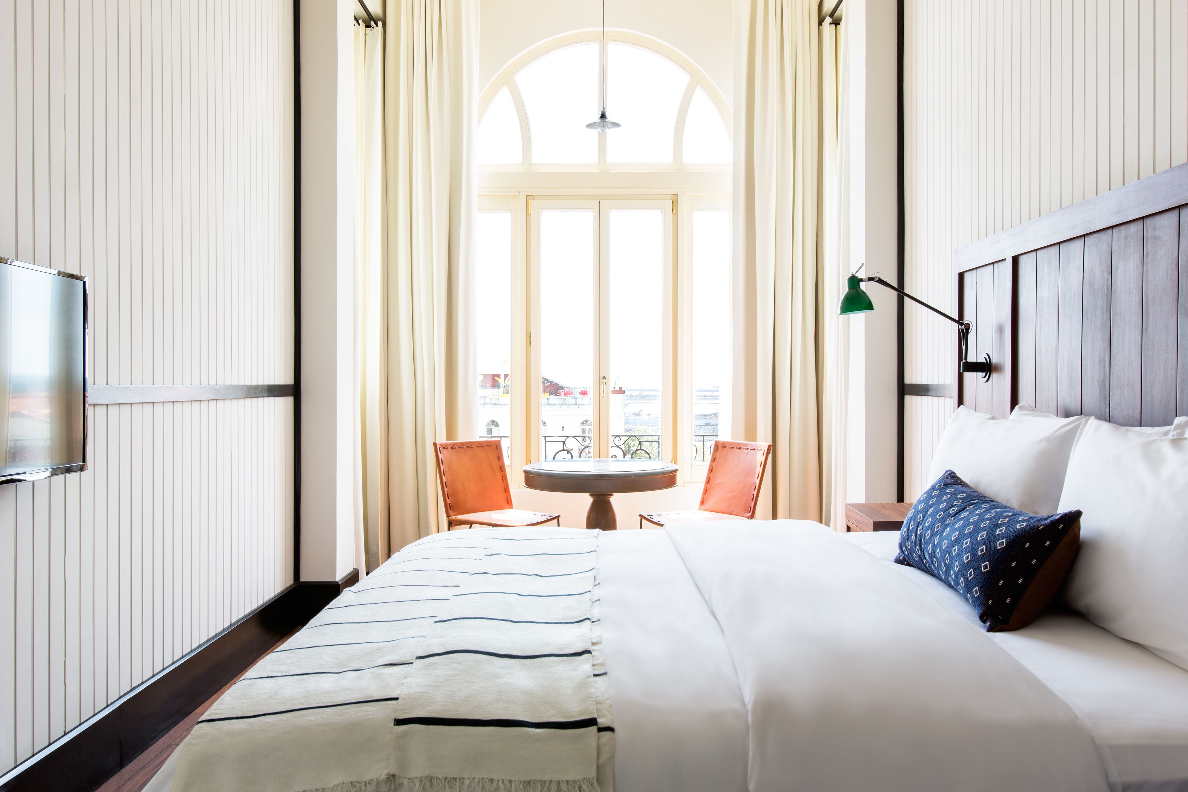 A hotel room with a bed, a TV, a table with chairs, and a view of the outside.