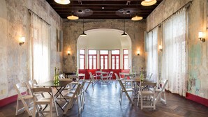 Un comedor amplio con suelo de madera en espiga, sillas blancas y mesas dispuestas alrededor de un sofá rojo central.