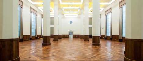 A spacious hallway with wooden flooring, large windows, and modern lighting fixtures.