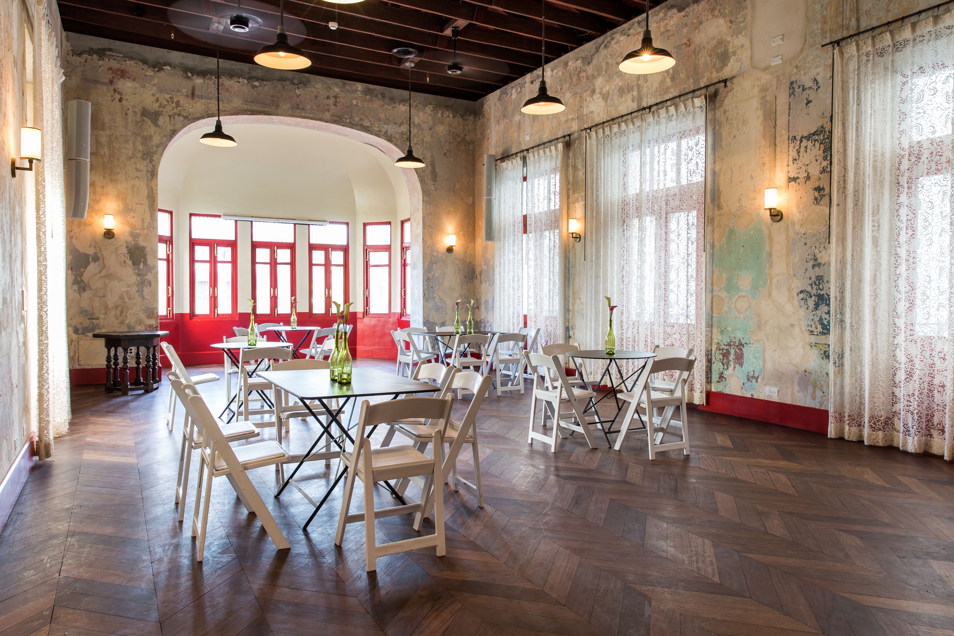 A spacious dining area with high ceilings, exposed brick walls, and large windows with red frames.