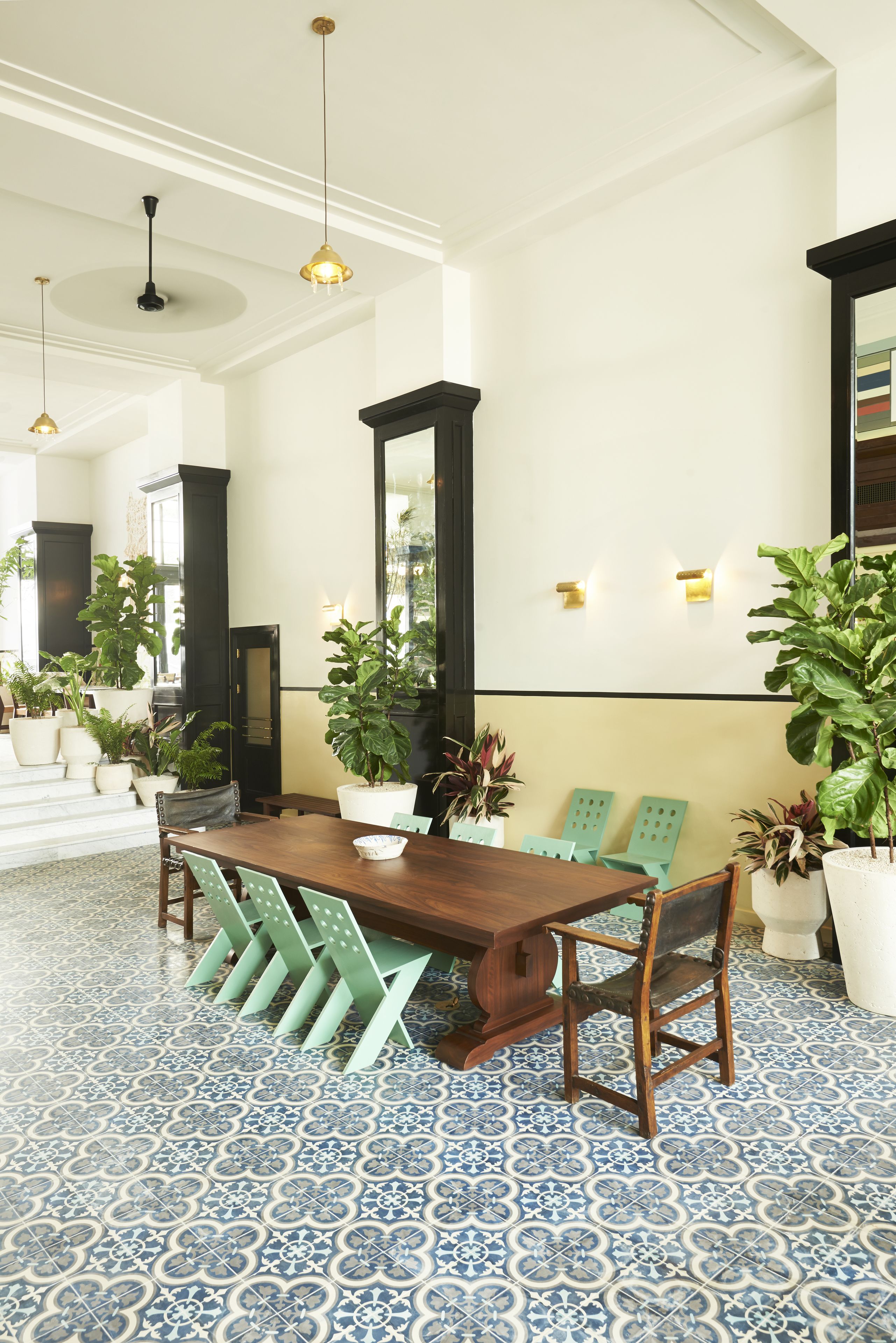 A dining area with a wooden table, green chairs, potted plants, and patterned floor tiles.