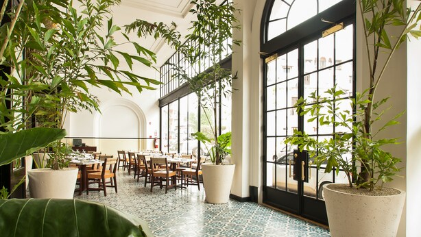 Un espacio interior amplio con techos altos, ventanas grandes y varias mesas de comedor.