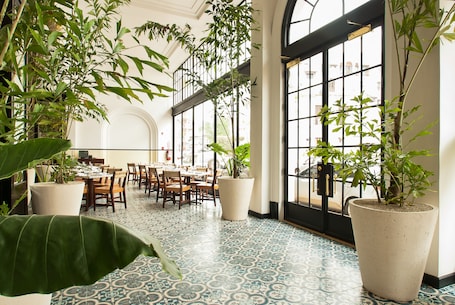 A spacious indoor area with high ceilings, large windows, and multiple dining tables.