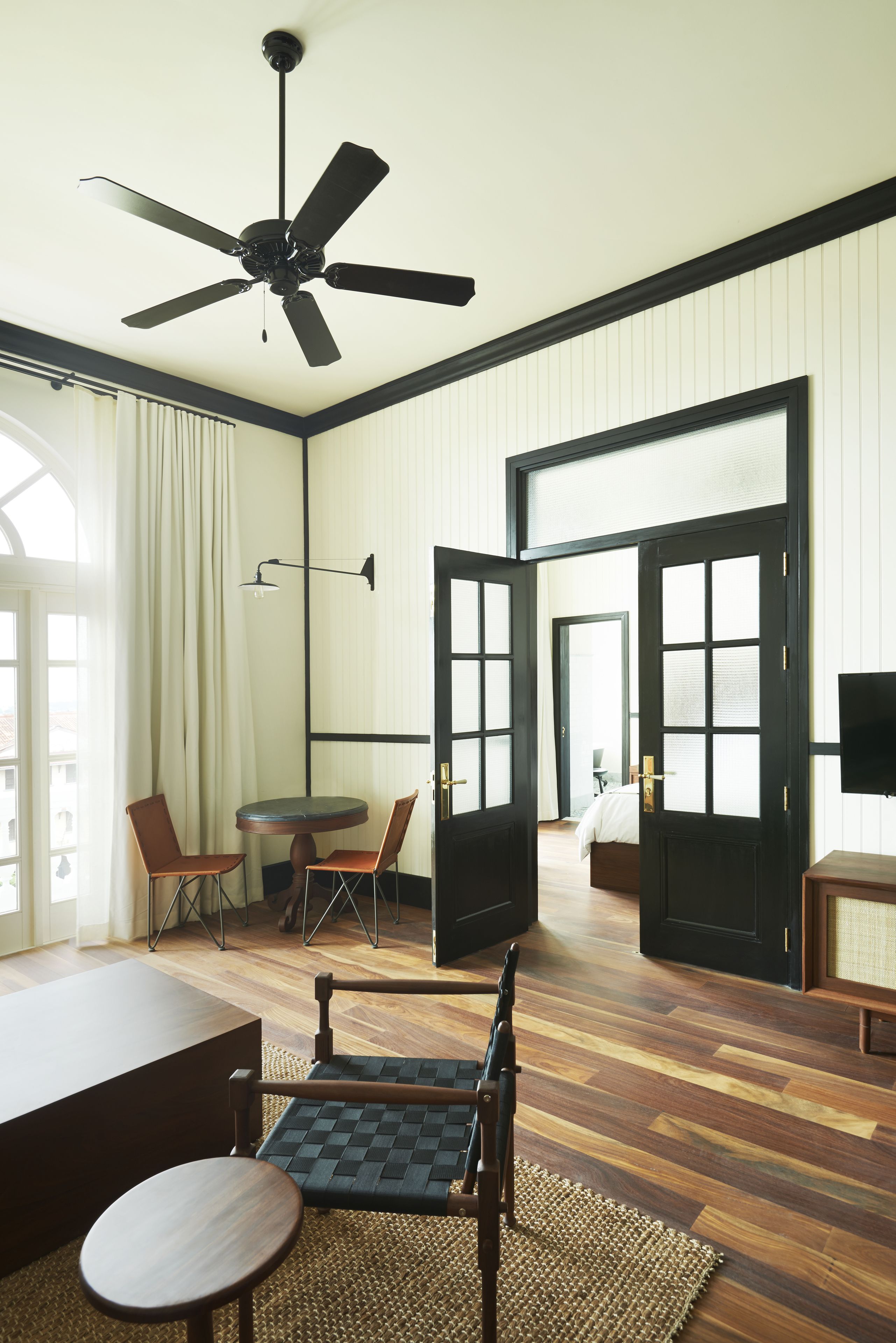 A hotel room with a ceiling fan, a round table with chairs, a bed, and a TV.