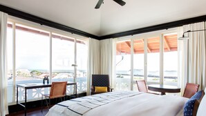 Habitación de hotel con una cama grande, un escritorio y un balcón con vistas a la ciudad.