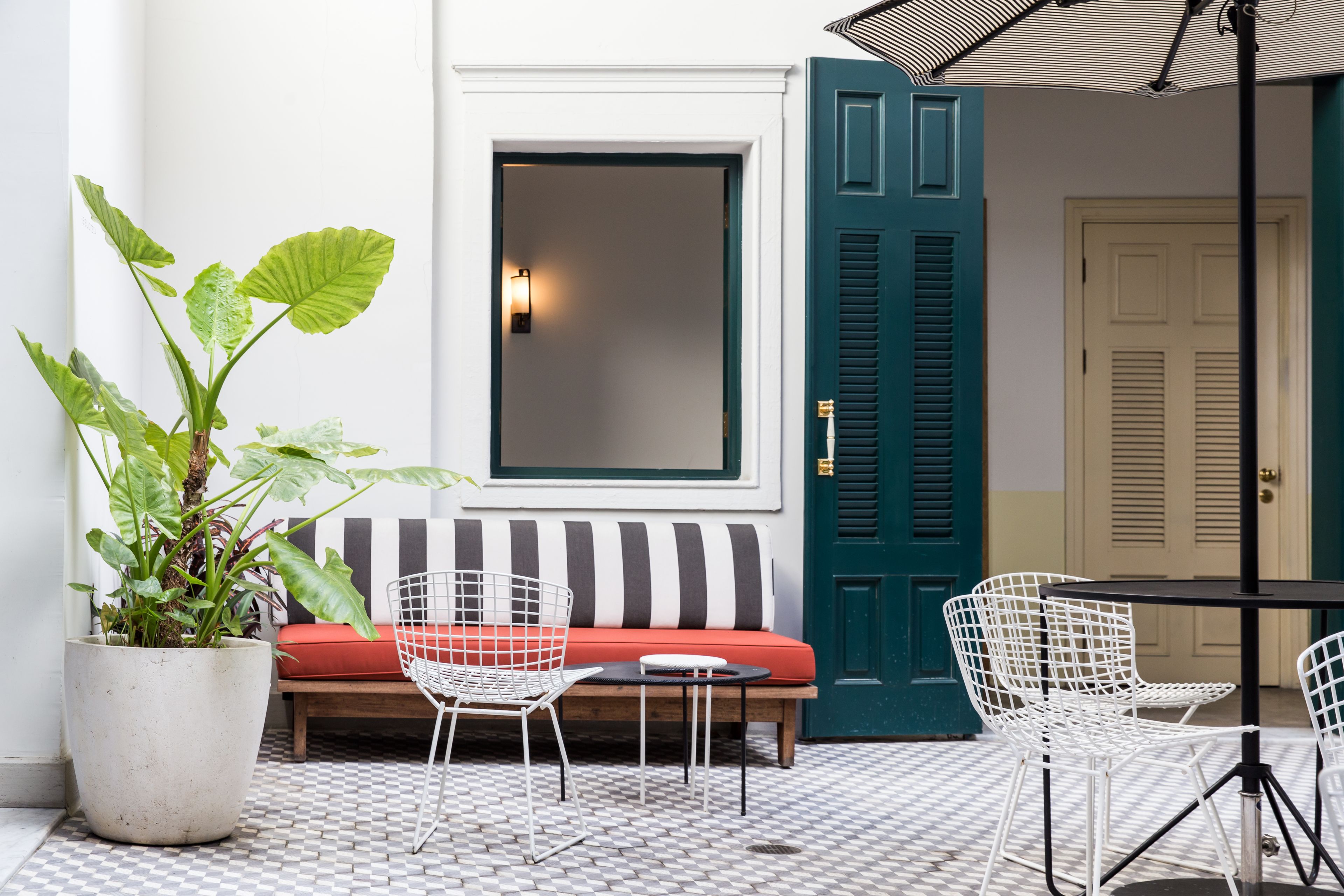 A cozy outdoor seating area with a checkered floor, a potted plant, a bench with red cushions, and a table with chairs.