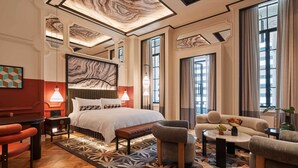 Una habitación de hotel con una cama grande, un sofá, una mesa de centro y un comedor con mesa y sillas.