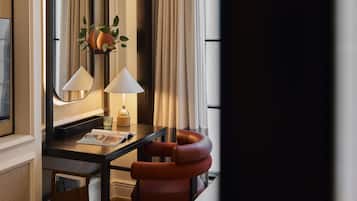 A modern hotel room with a dark wood desk, two lamps, a mirror, and a red chair.