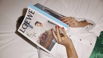 A person lying on a bed, holding a magazine titled "LOFWE".