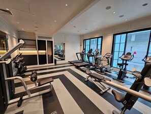 Un gimnasio moderno con diversos equipos de ejercicio, amplias ventanas y un interior limpio y bien iluminado.