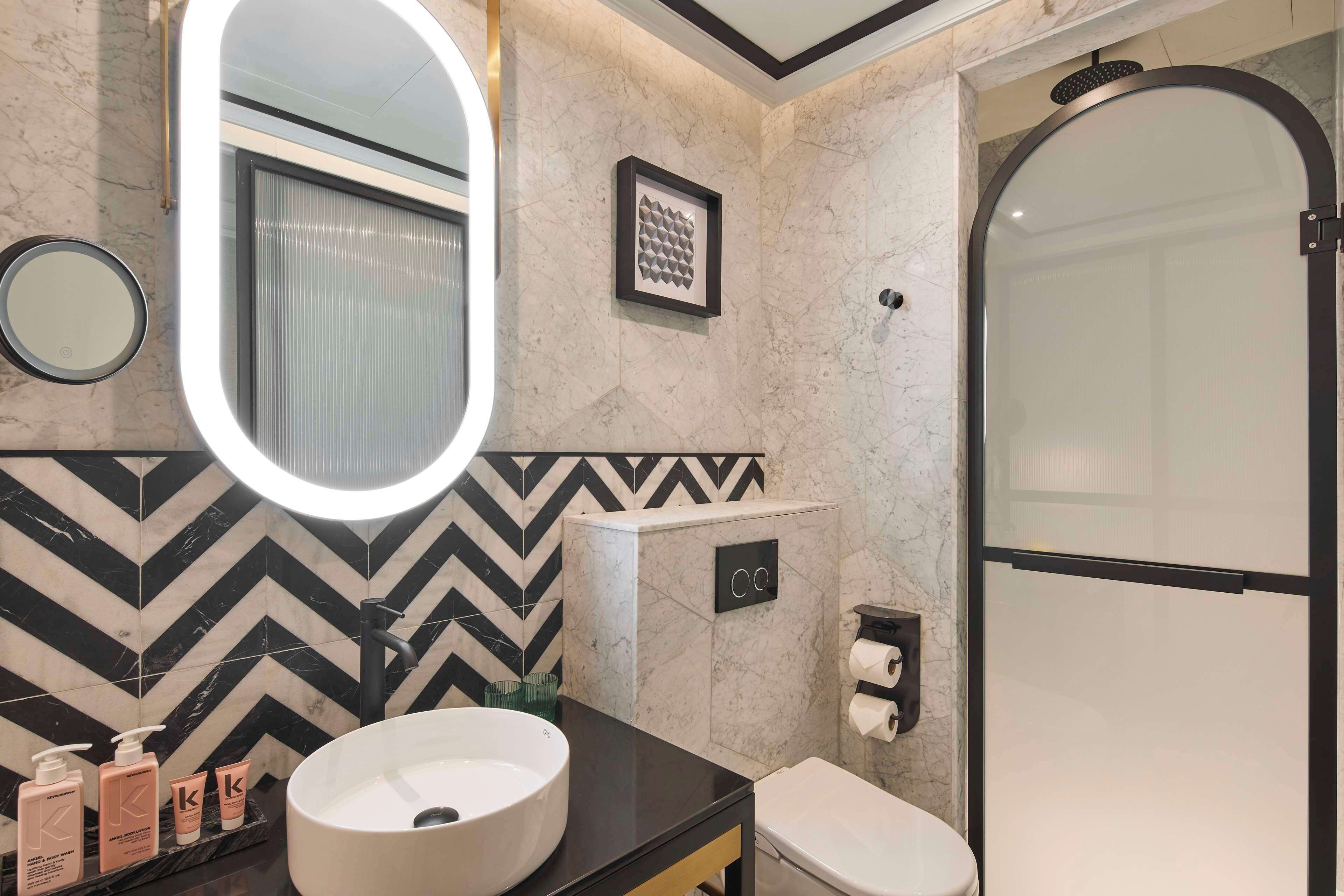 A modern bathroom with a black and white tile backsplash, a large mirror, a round sink, a toilet, and a shower enclosure.