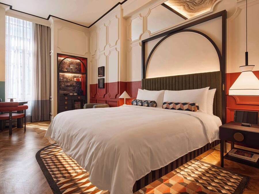 A hotel room with a large bed, a desk, a chair, a TV, and a bookshelf.