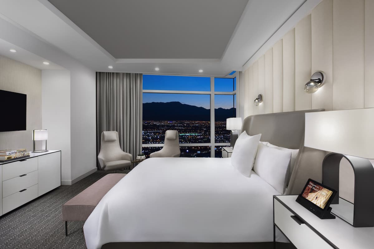Habitación de hotel moderna con una cama grande, un escritorio, un televisor de pantalla plana y vistas a la ciudad desde la ventana.