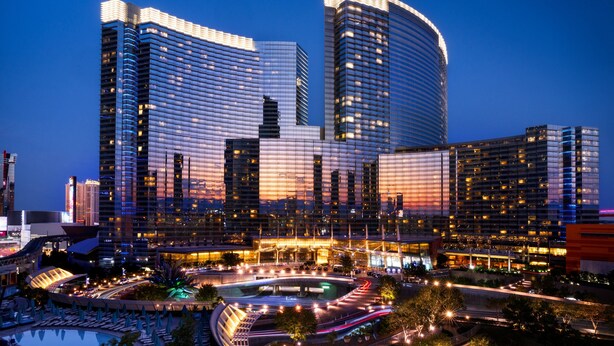 A modern hotel with a curved facade, multiple high-rise buildings, and a well-lit pool area. - ARIA Sky Suites (Las Vegas)