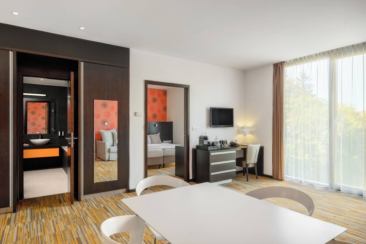 Ein Hotelzimmer mit einem großen Bett, einem Schreibtisch mit Stuhl, einem Fernseher und einem Esstisch.