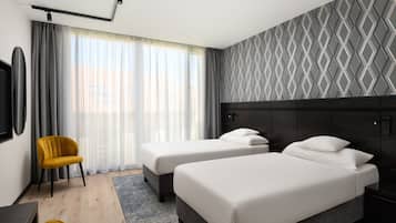 A hotel room with two beds, a yellow chair, a TV, and a patterned wall.