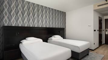 A hotel room with two single beds, a dark headboard, a geometric patterned wall, and a door to the right.