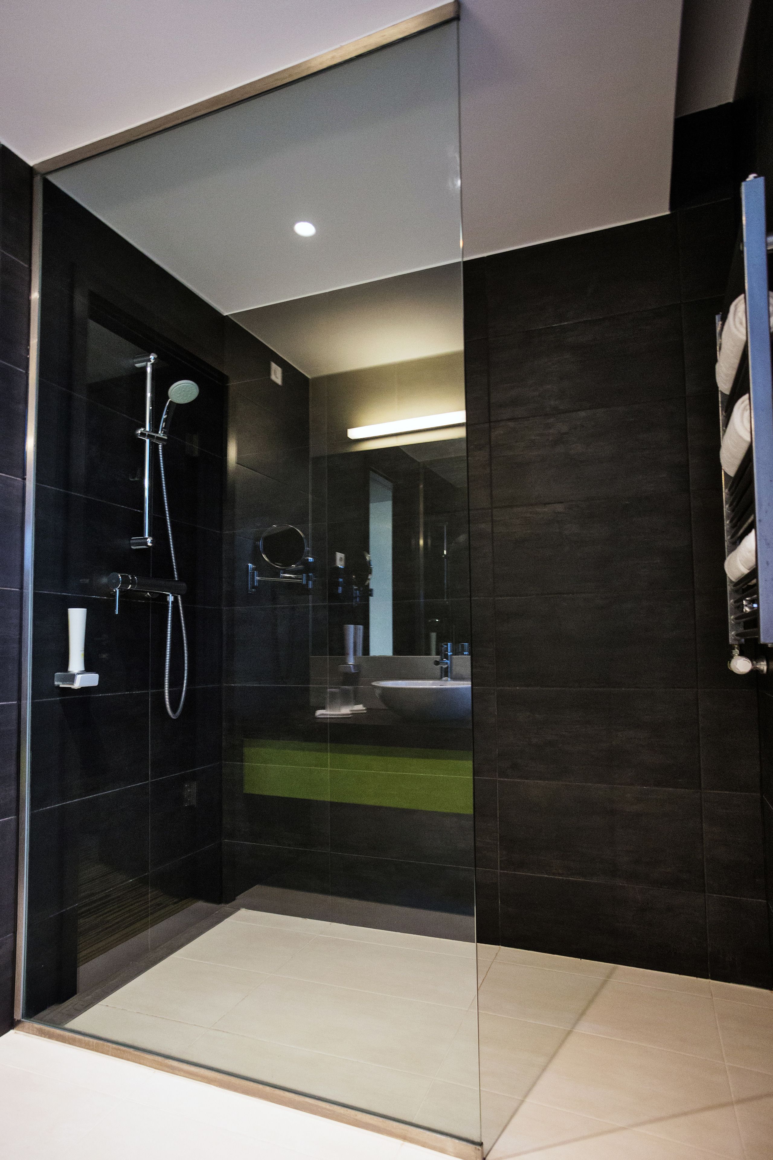 Een moderne badkamer met een douchecabine van glas, donkere tegels en een zichtbaar wastafelgedeelte.