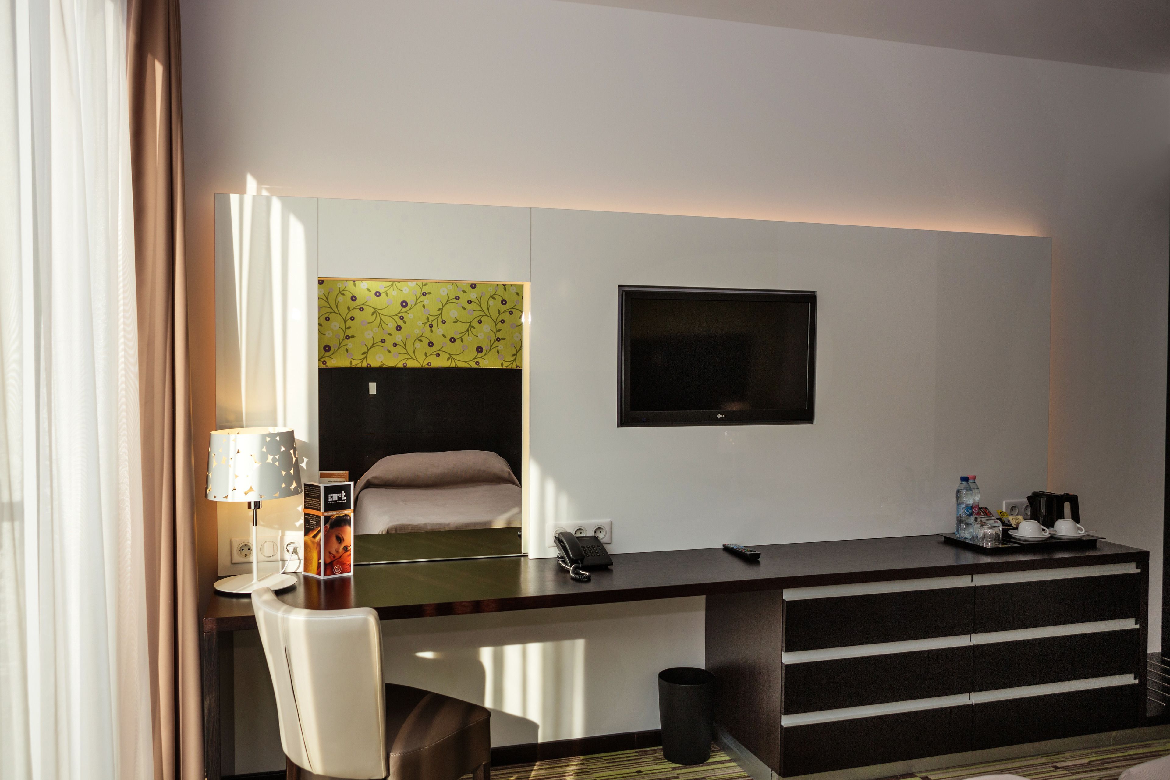 A modern hotel room with a desk, chair, and a TV mounted on the wall.