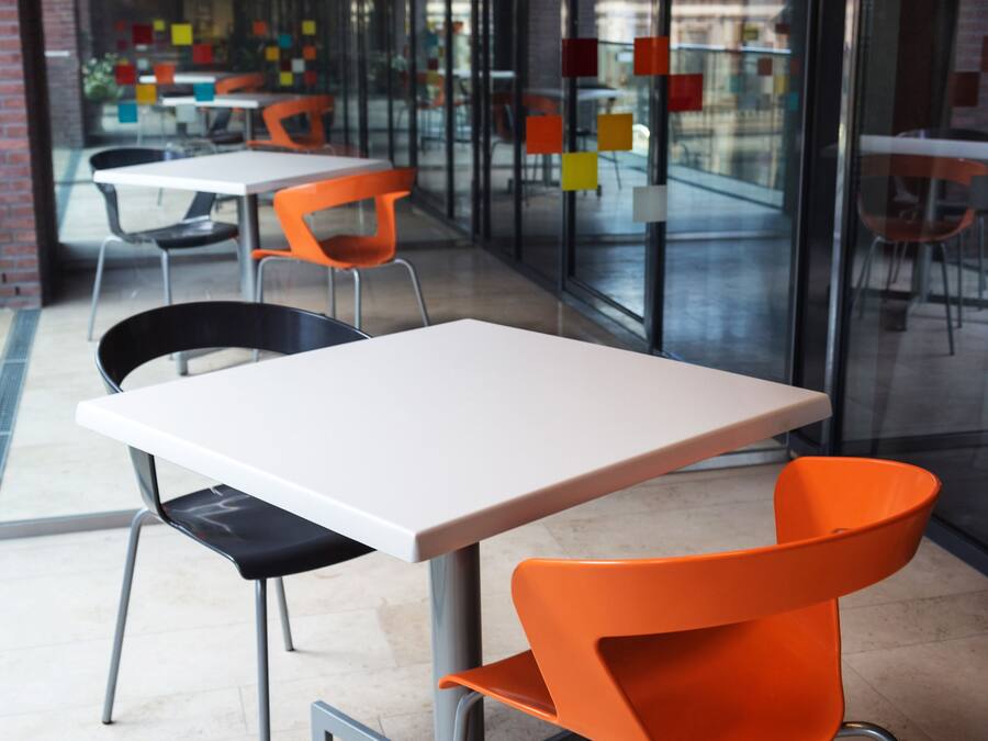 A modern indoor space with glass walls, a white table, and orange chairs.