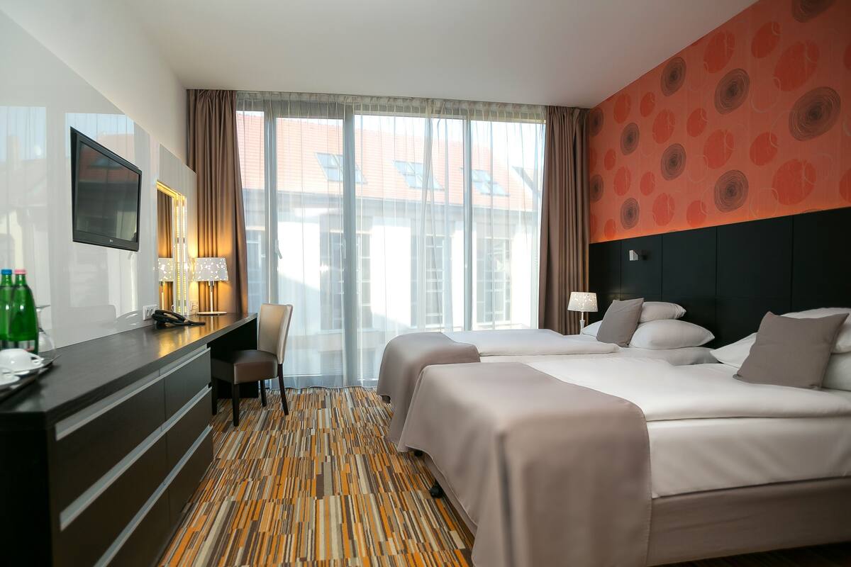 Ein Hotelzimmer mit Schreibtisch, zwei Betten, einem Fernseher und einem großen Fenster mit Vorhängen.