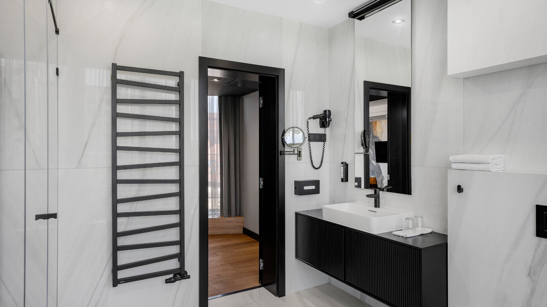 A modern bathroom with a black vanity, a large mirror, and a towel rack.