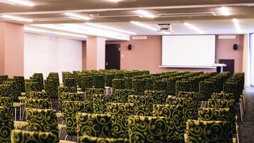 Filas de sillas estampadas en verde en una sala de conferencias con una pantalla de proyector y una pizarra.
