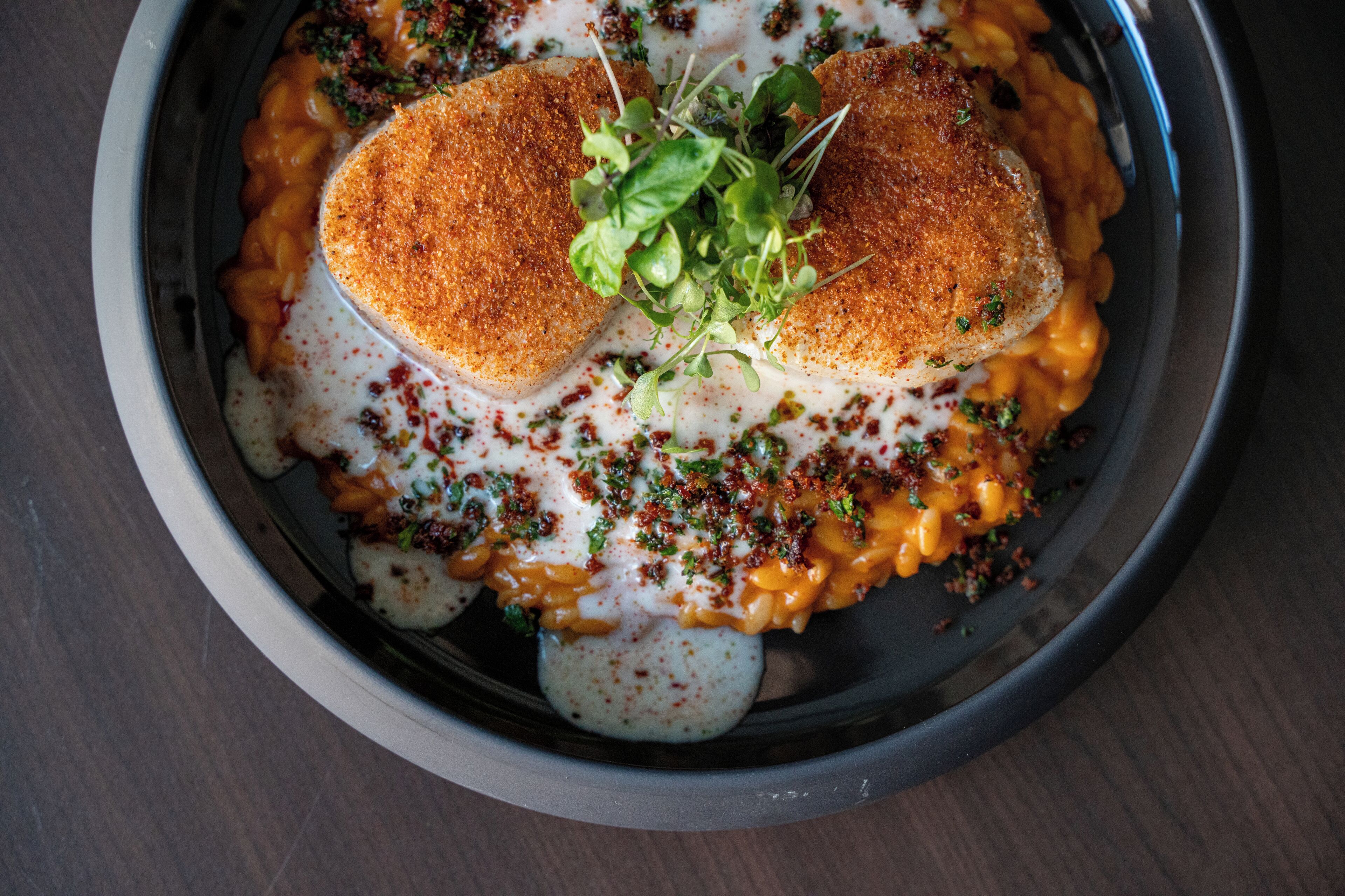 A bowl of food with two pieces of breaded chicken, macaroni, and a creamy sauce, garnished with herbs.