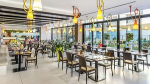 Un restaurante moderno con varias mesas y sillas, ventanas amplias y lámparas colgantes.