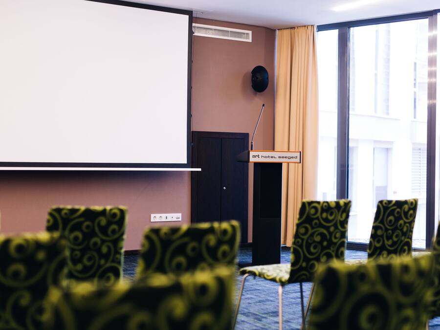 Un salón de conferencias con una pantalla de proyector, un atril y sillas estampadas.